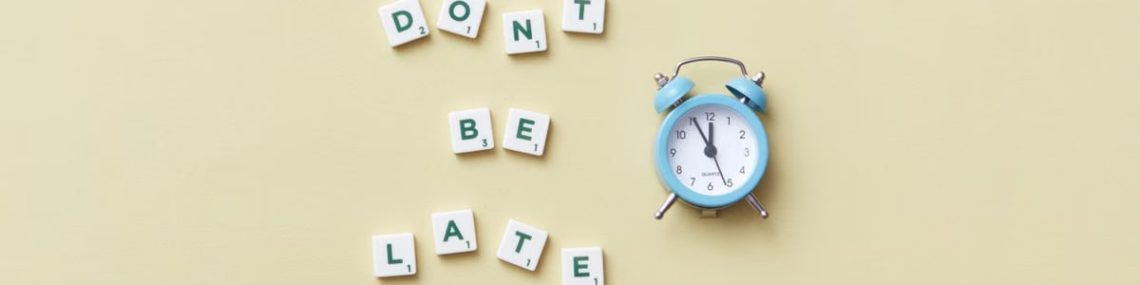 Flat lay of a blue alarm clock and letter tiles spelling 'Don't Be Late'.